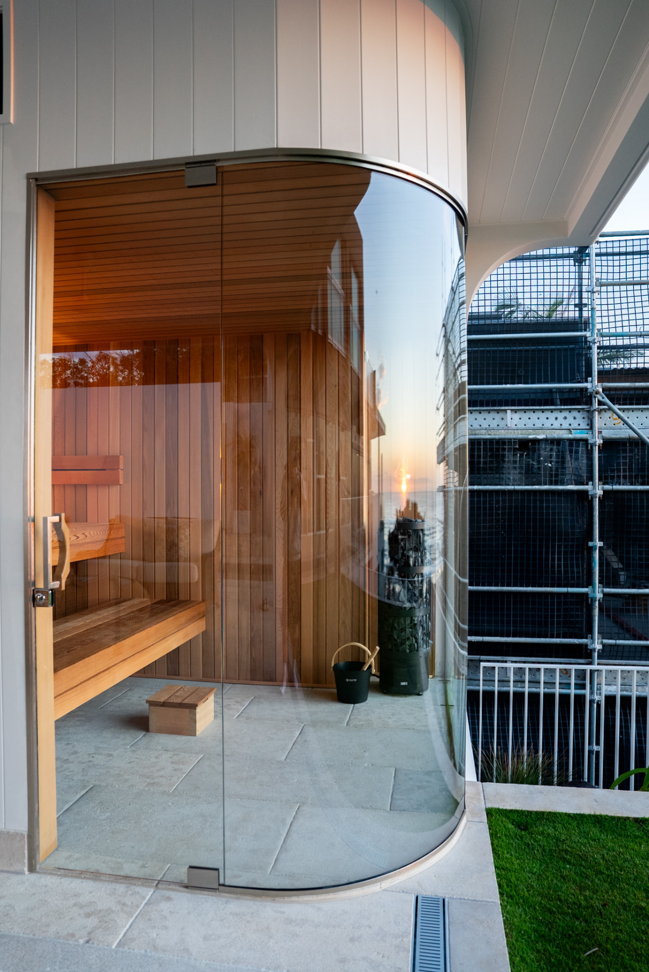 Curved glass sauna entrance with warm timber benches