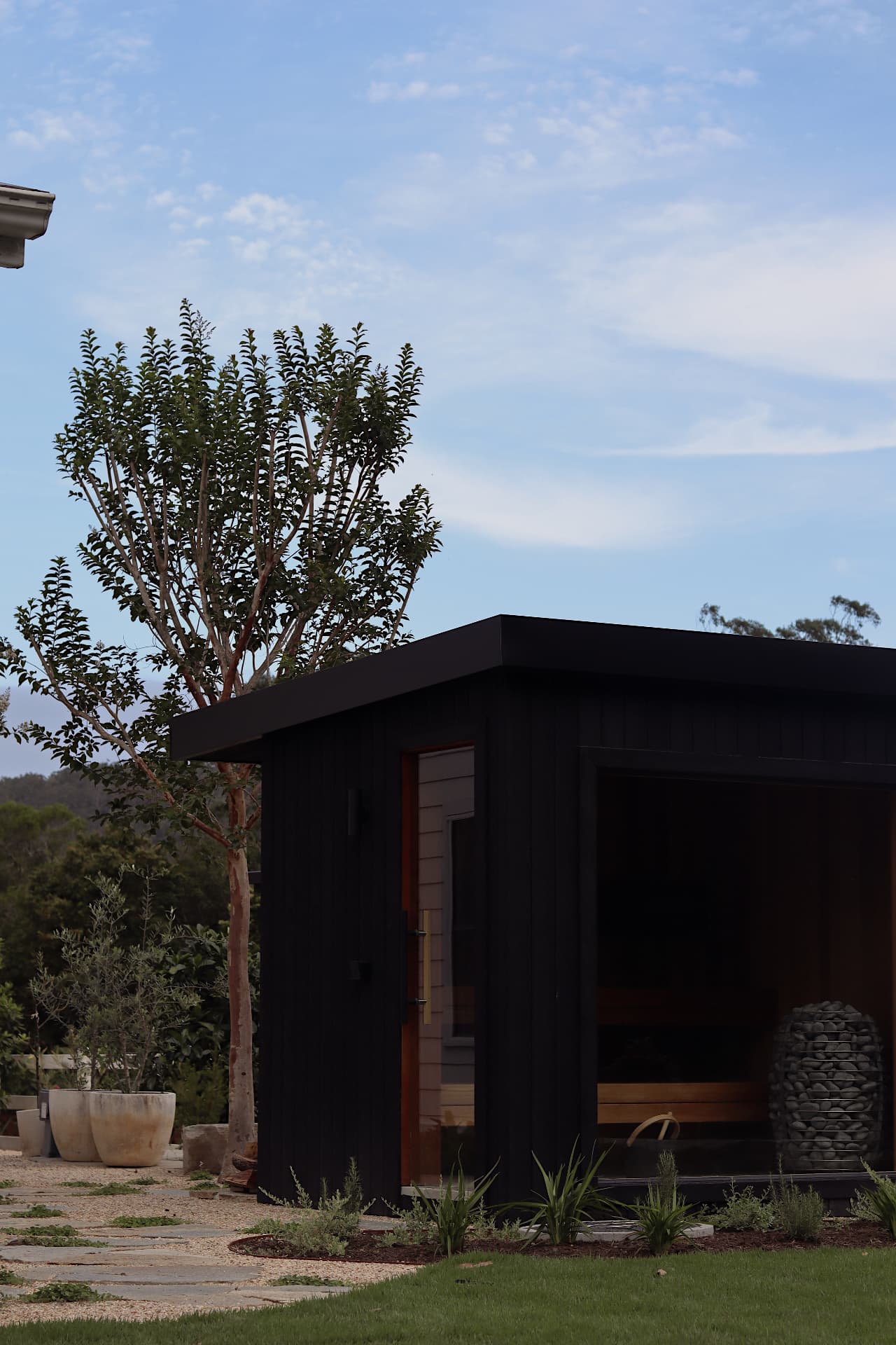 Freestanding dark timber sauna beside a landscaped garden