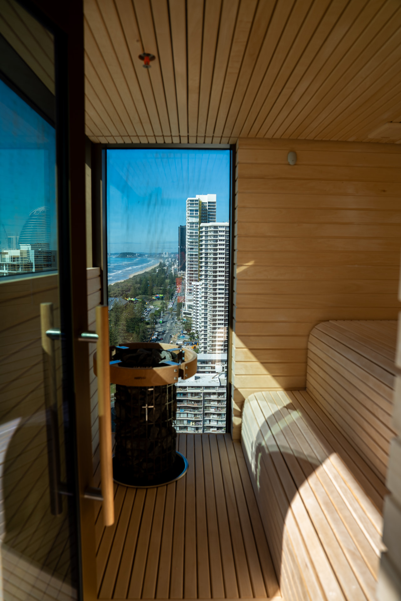 Timber sauna with a tall stone heater and floor-to-ceiling glazing