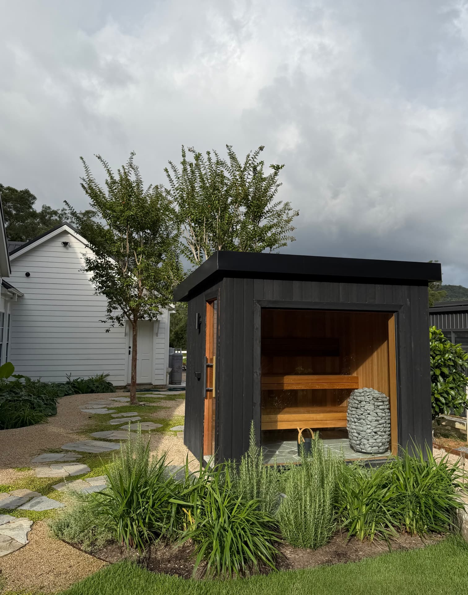 Dark timber garden sauna with glass front and landscaped planting